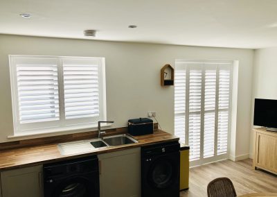 Plantation shutters in a kitchen, white full height interior window shutters and sliding track patio door shutters,